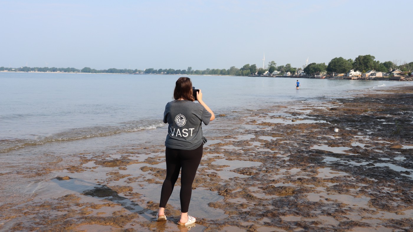 Photo of Citizen Scientist Using VAST- Wearing a grey tshirt, standing by Lake Erie beach shoreline