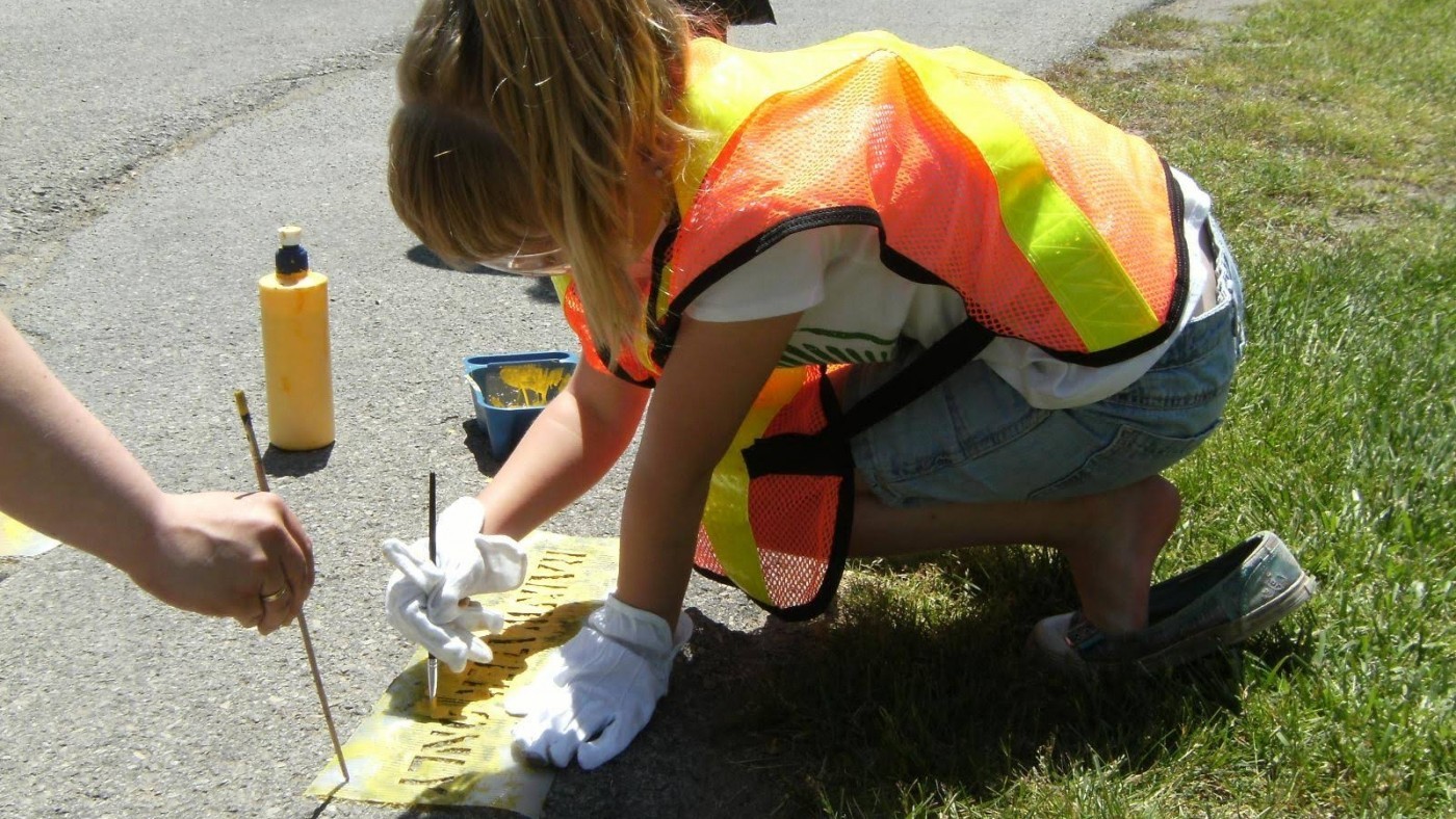 Young girl painting yellow fish near storm drain