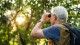 Man looks towards trees with binoculars. 