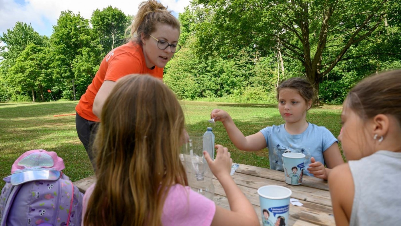Outdoor Educator, Jenna Moorhead dressed in orange, teaches children about nature through experiments.