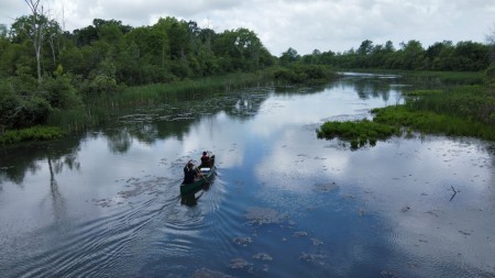 NPCA Staff on a canoe on Lyons Creek East in Welland, blue water and clear skies surrounded by trees