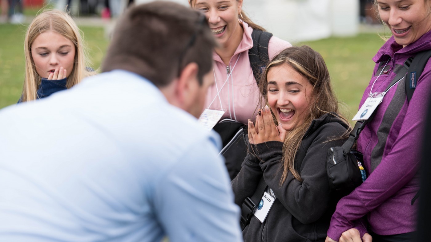 A group of four girls showing diverse reactions, including surprise and intrigue, to something happening out of view.