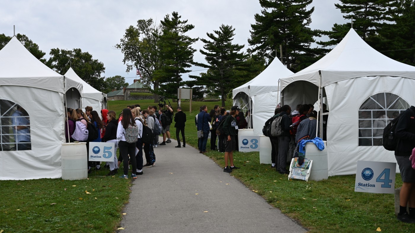 Large white tents line a sidewalk, with groups of students gathered at each one.