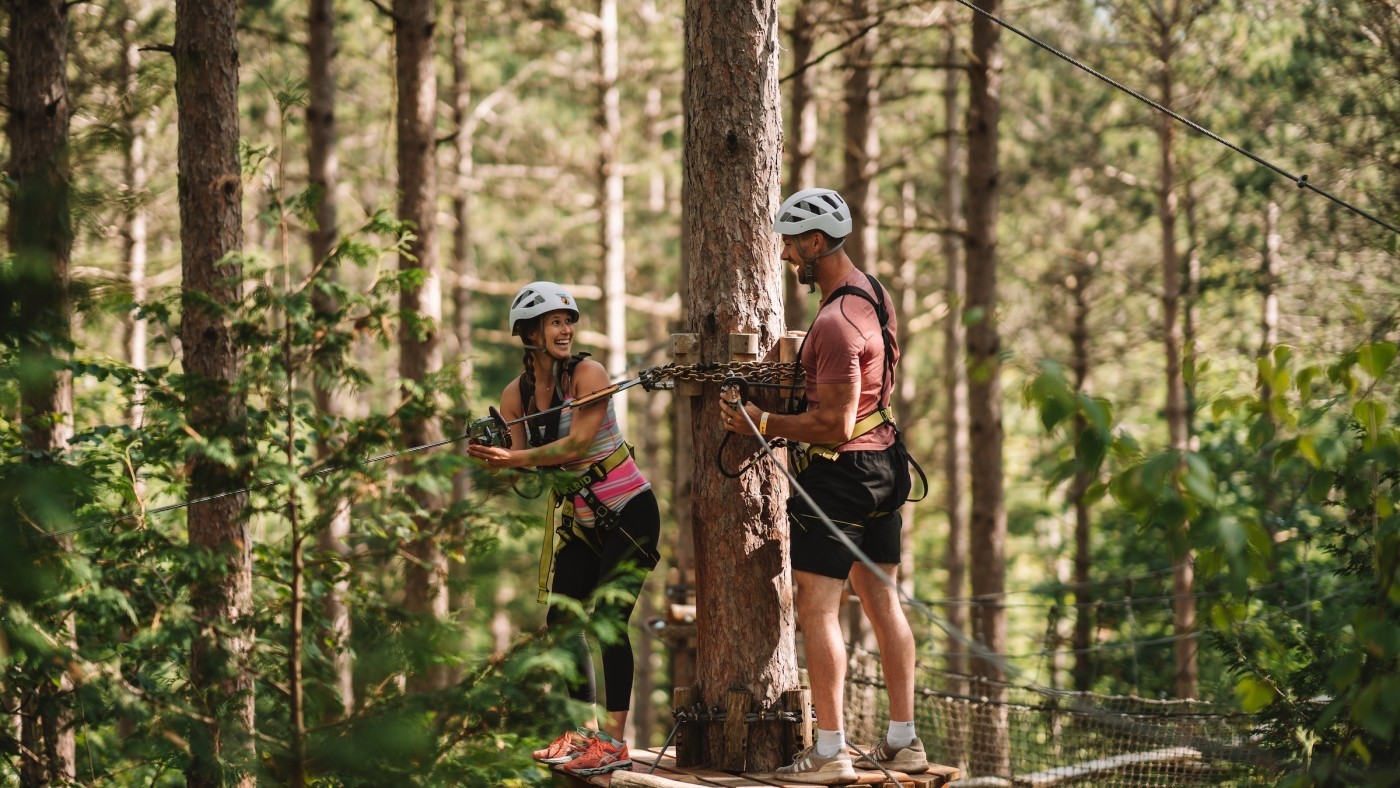 Photo of two people on Treetop Trekking adventure surrounded by green trees, brown branches