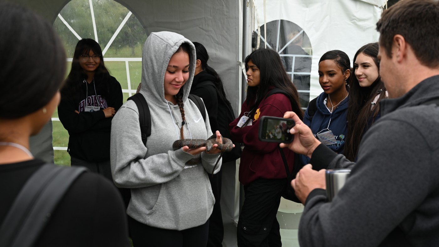 A student holds a snake while classmates gather around and take pictures.